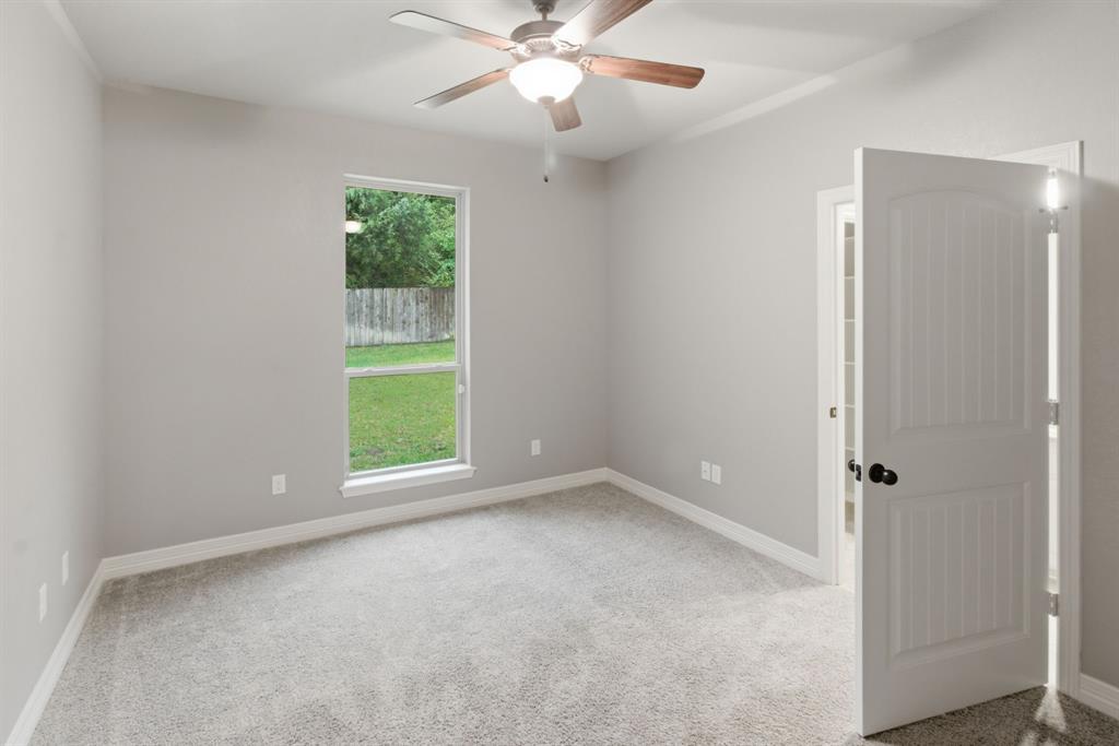 7765 Hickory Spring Lane Tyler, TX 75703 - Photo 30 of 38 Neutral-toned room featuring a ceiling fan with integrated lighting, a backyard window overlooking greenery and a wooden fence, plush grey carpeting, and a paneled interior door with matte black hardware