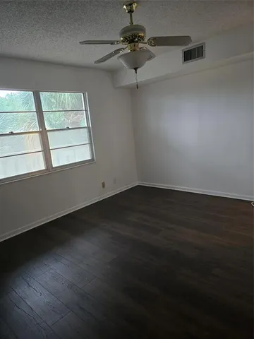 an empty room with wooden floor fan and windows