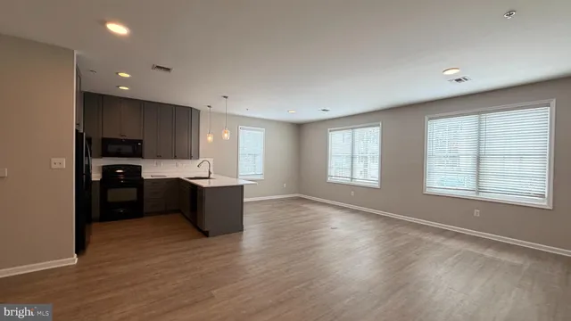 a large kitchen with stainless steel appliances granite countertop a large counter top a wooden floors and a large window