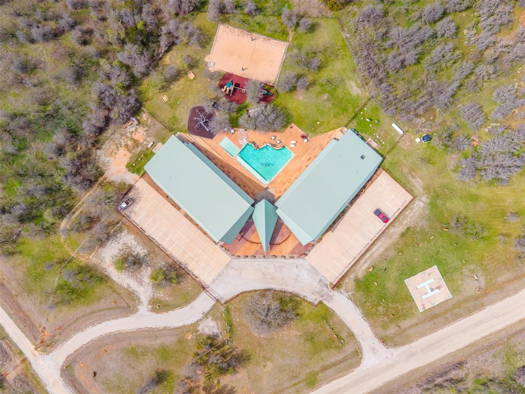E49 R Art's Way Gordon, TX 76453 - Photo 23 of 26 Aerial view showcasing a sprawling property featuring a central building with a light green roof, a swimming pool, extensive paved patio areas, and surrounding natural landscaping