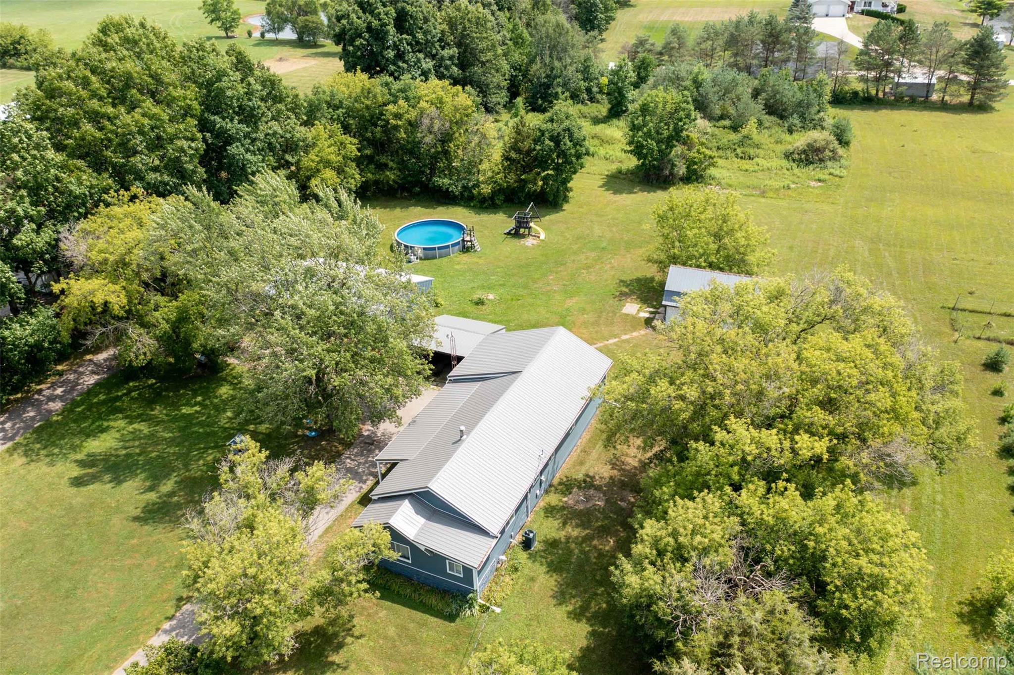 5761 Genesee Road Lapeer, MI 48446 - Photo 38 of 52 Spacious property featuring a blue-sided residence with a gray metal roof, surrounded by mature trees and expansive green areas