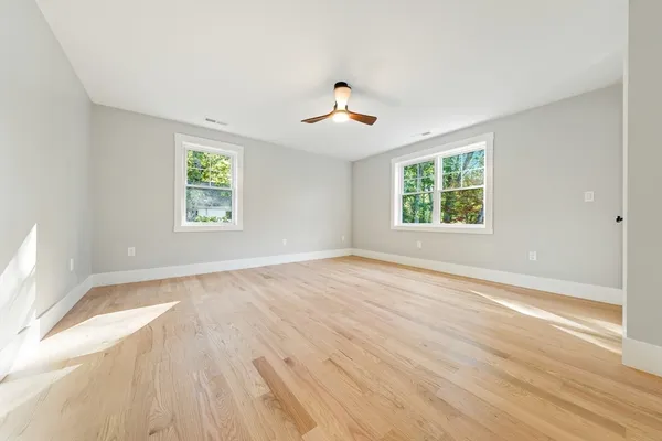 an empty room with wooden floor ceiling fan and windows