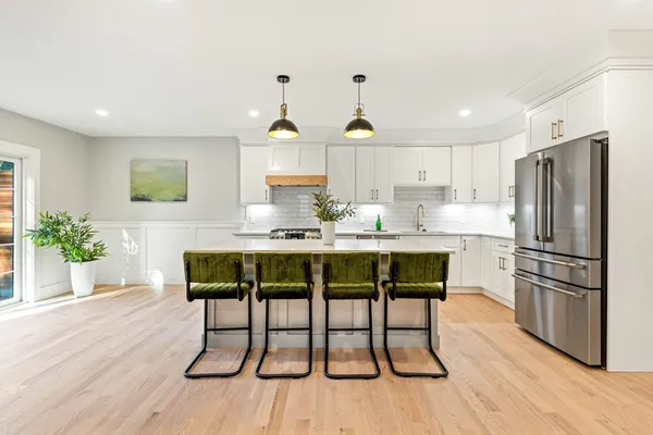 a kitchen with stainless steel appliances granite countertop a dining table chairs refrigerator and sink
