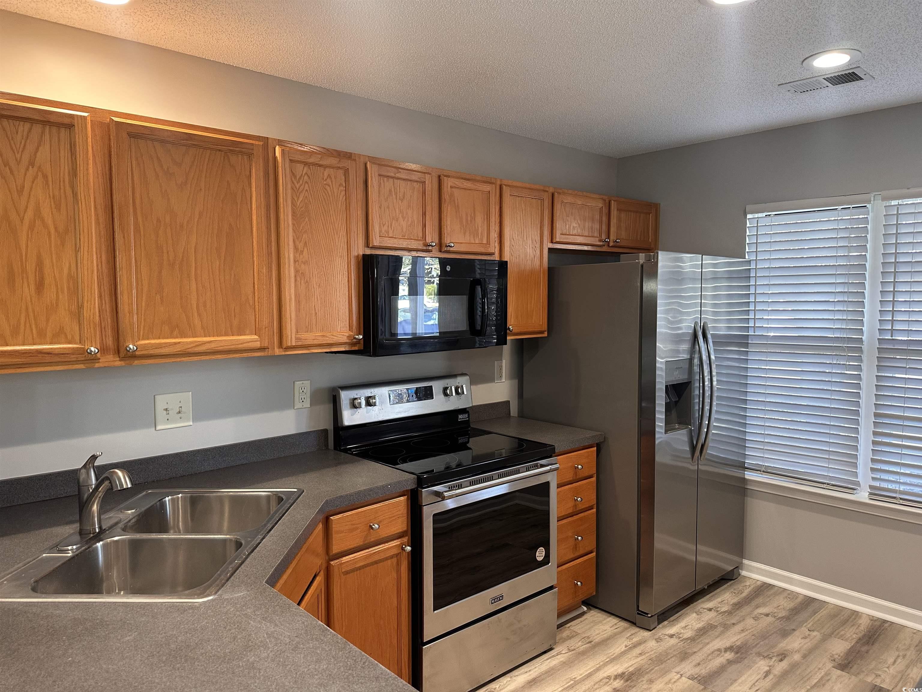 257 Seabert Road Myrtle Beach, SC 29579 - Photo 3 of 16 Kitchen with appliances with stainless steel finishes, a textured ceiling, dark countertops, brown cabinetry, and light wood-type flooring