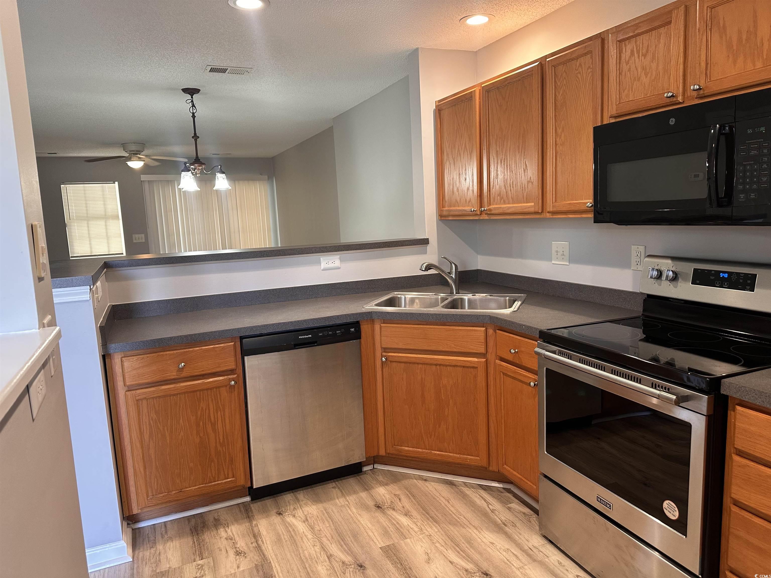 257 Seabert Road Myrtle Beach, SC 29579 - Photo 4 of 16 Kitchen with appliances with stainless steel finishes, dark countertops, brown cabinetry, light wood-style floors, and a textured ceiling