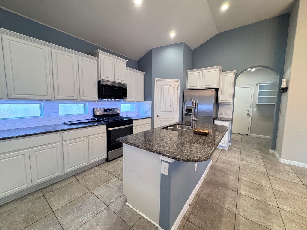 16420 Pienza Drive Pflugerville, TX 78660 - Photo 8 of 26 Kitchen with appliances with stainless steel finishes, a center island with sink, decorative backsplash, vaulted ceiling, and light tile patterned floors