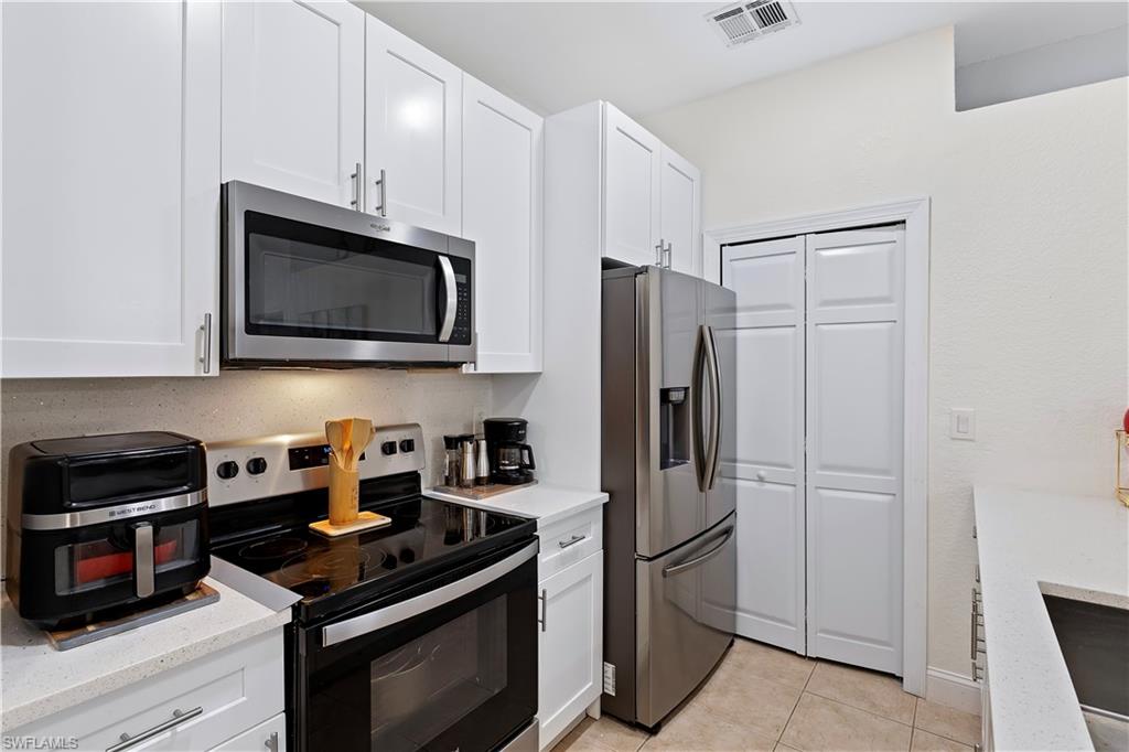 7542 Bristol Circle Naples, FL 34120 - Photo 5 of 26 Kitchen with white cabinets, stainless steel appliances, light tile patterned flooring, and light stone countertops
