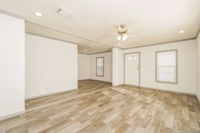 a view of an empty room with chandelier fan and wooden floor