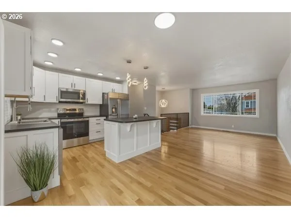a kitchen with stainless steel appliances granite countertop a refrigerator a sink dishwasher a oven with white cabinets and wooden floor