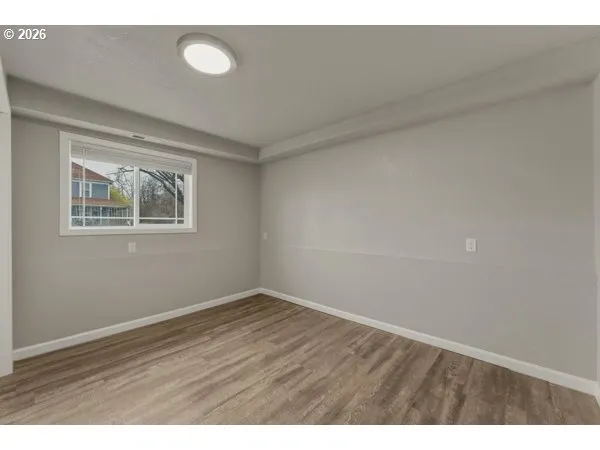 a view of an empty room with wooden floor and a window