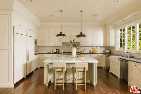 a kitchen with stainless steel appliances kitchen island a table chairs in it white cabinets and a floors