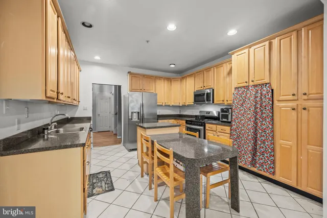 a kitchen with stainless steel appliances granite countertop a refrigerator a stove a sink a dining table and chairs with the cabinets