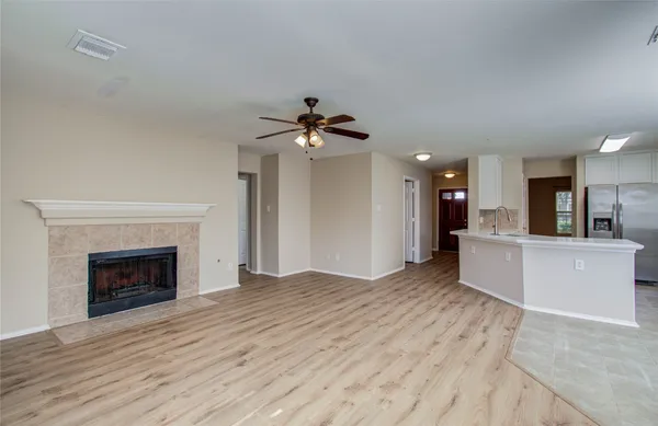 a view of an empty room and kitchen with fireplace ceiling fan