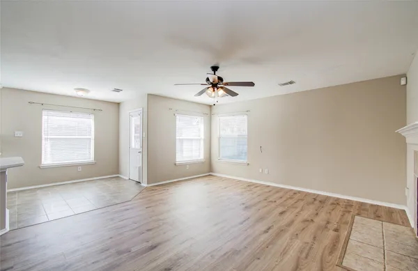 an empty room with wooden floor chandelier fan and windows