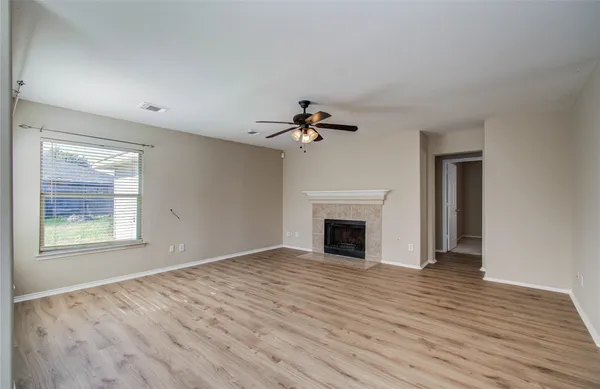 a view of an empty room with wooden floor fireplace and a window