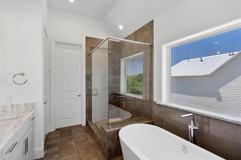 1362 East Crosby Road Carrollton, TX 75006 - Photo 14 of 22 Contemporary bathroom featuring a freestanding soaking tub, a frameless glass shower enclosure, a dual-pane window, and a vanity with a light-colored countertop