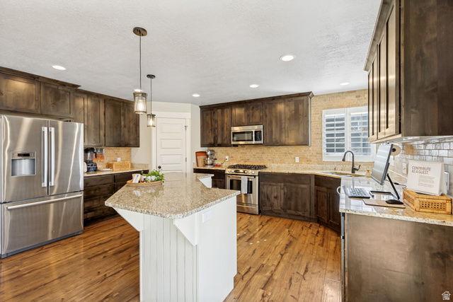 Wood-finish flooring with dark wood cabinetry, stainless steel appliances, and a central island with a light-toned countertop