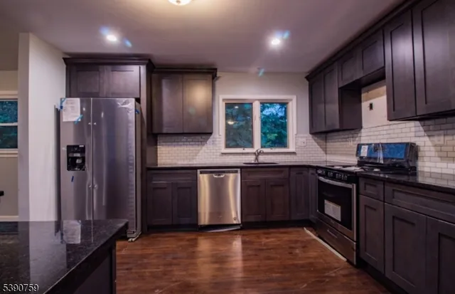 a kitchen with stainless steel appliances granite countertop wooden cabinets a refrigerator a sink a stove a counter space and cabinets