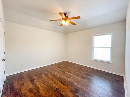 an empty room with wooden floor fan and windows