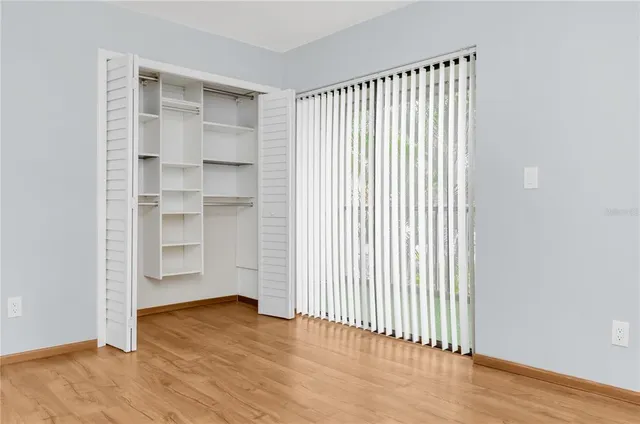 an empty room with wooden floor closet and windows