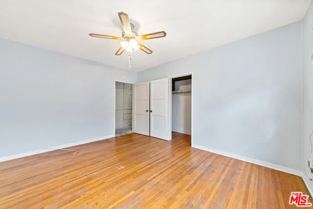 a view of an empty room with wooden floor and a ceiling fan