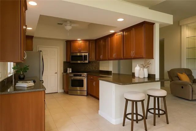 a kitchen with stainless steel appliances kitchen island granite countertop a stove a sink a refrigerator white cabinets and chairs