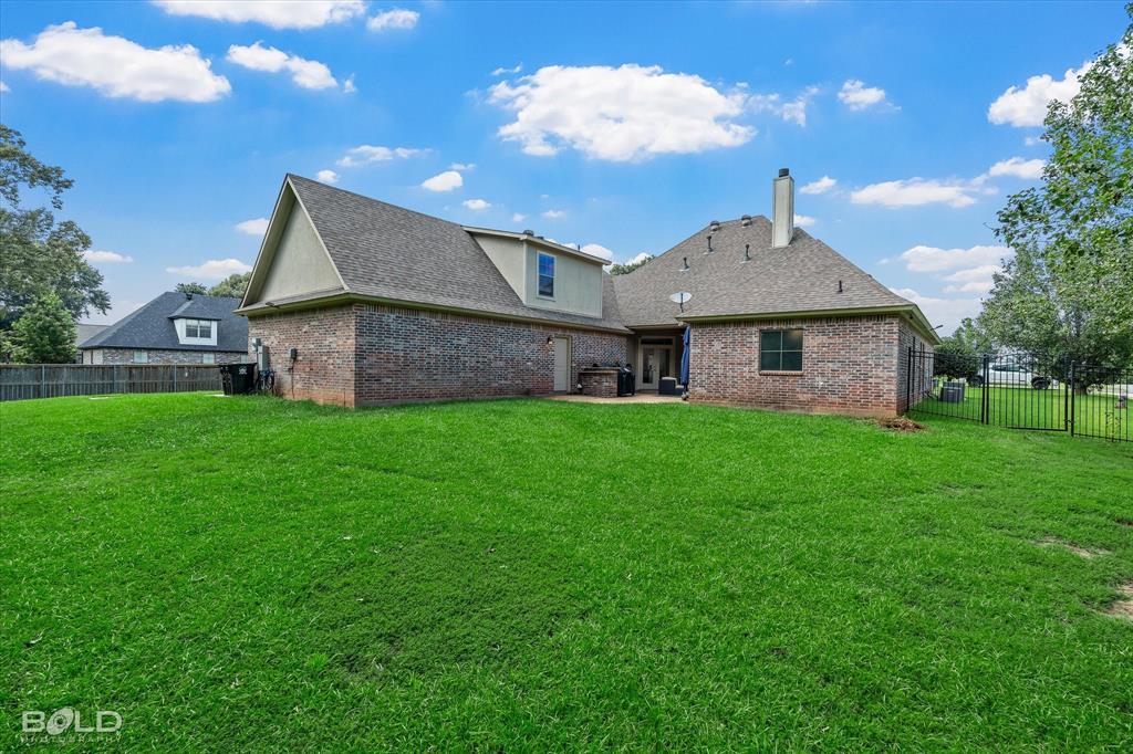 2220 Forest Hills Boulevard Haughton, LA 71037 - Photo 4 of 40 Expansive green lawn bordering a brick exterior residence featuring a gabled roofline and a rear patio