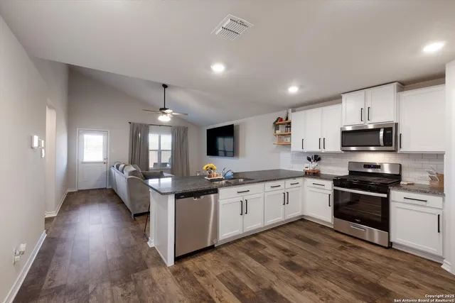 a kitchen with stainless steel appliances granite countertop a stove top oven a sink dishwasher a refrigerator and white cabinets with wooden floor