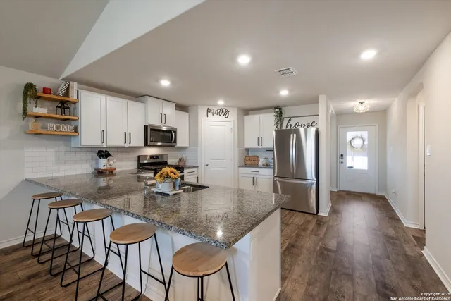 a kitchen with stainless steel appliances granite countertop a refrigerator a stove a sink a dining table and chairs with wooden floor