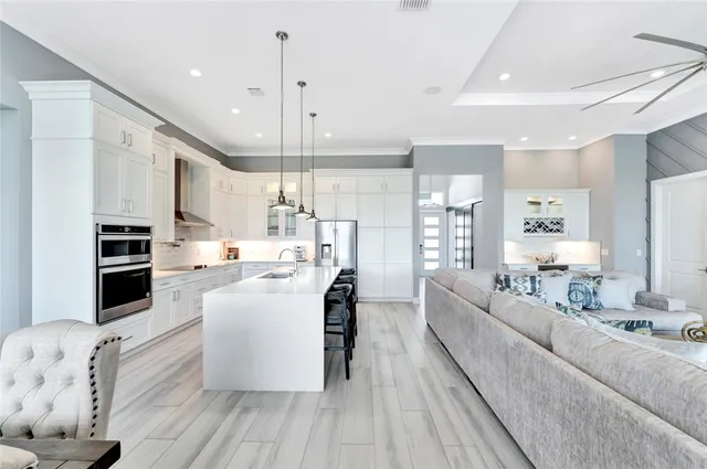 a large white kitchen with stainless steel appliances kitchen island a large counter top a couch a stove and a refrigerator