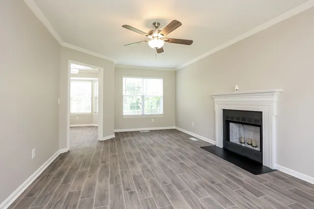 an empty room with wooden floor a ceiling fan and windows