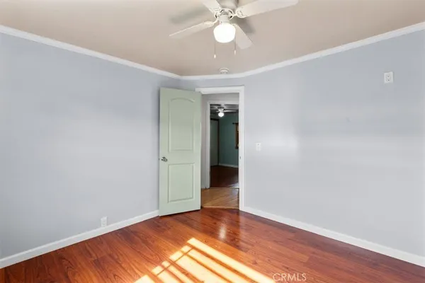 a view of an empty room with wooden floor and a ceiling fan
