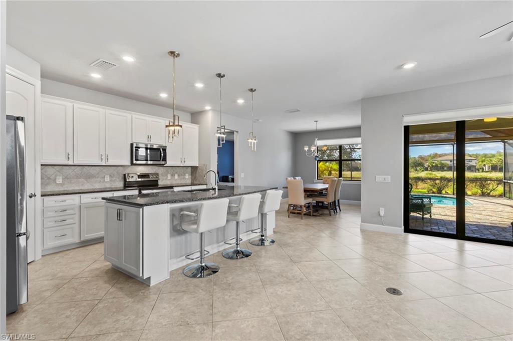 19902 Beverly Park Road Estero, FL 33928 - Photo 8 of 47 Kitchen with a breakfast bar area, a kitchen island with sink, decorative light fixtures, dark stone counters, and appliances with stainless steel finishes