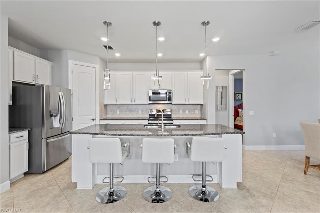 19902 Beverly Park Road Estero, FL 33928 - Photo 9 of 47 Kitchen featuring dark stone counters, a kitchen bar, hanging light fixtures, stainless steel appliances, and white cabinetry