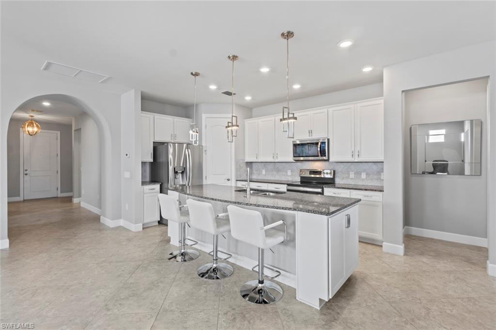 19902 Beverly Park Road Estero, FL 33928 - Photo 10 of 47 Kitchen featuring white cabinetry, a kitchen bar, dark stone counters, appliances with stainless steel finishes, and a kitchen island with sink