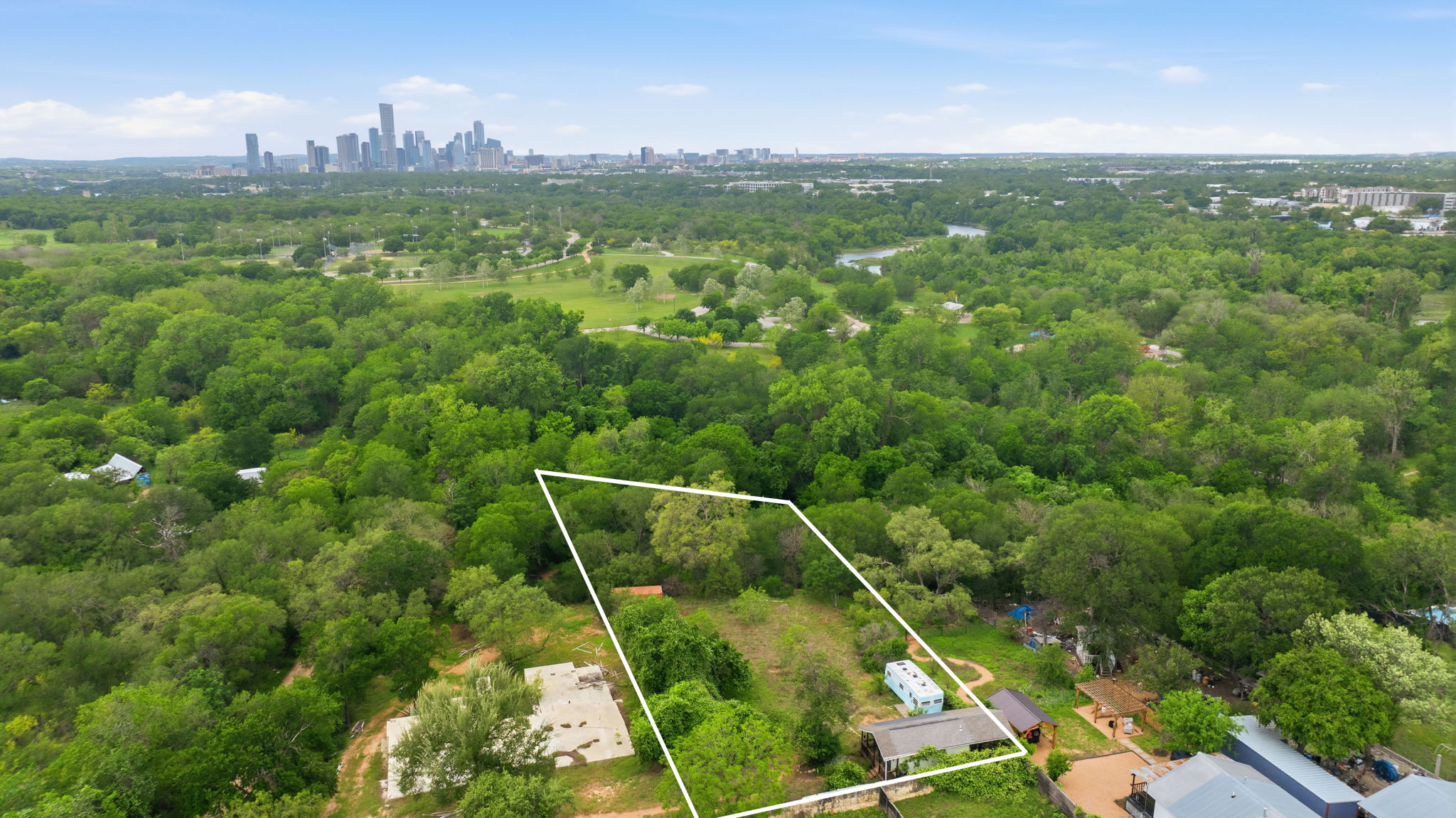 416 Kemp Street Austin, TX 78741 - Photo 3 of 14 Expansive parcel featuring a dense tree canopy, a visible concrete foundation, and a partial view of a distant urban skyline