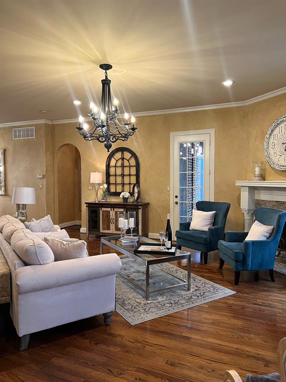 1625 Roma Lane Allen, TX 75013 - Photo 3 of 10 Spacious living area featuring wood-finish flooring, a decorative fireplace with a stone surround, and an elegant chandelier