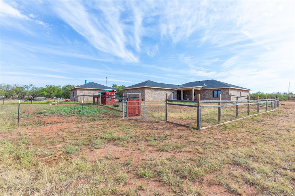 760 Wimberly Road Merkel, TX 79536 - Photo 3 of 35 Brick exterior residence with dark shingle roofing, featuring a covered patio, fenced yard area, and an additional red-painted shed structure