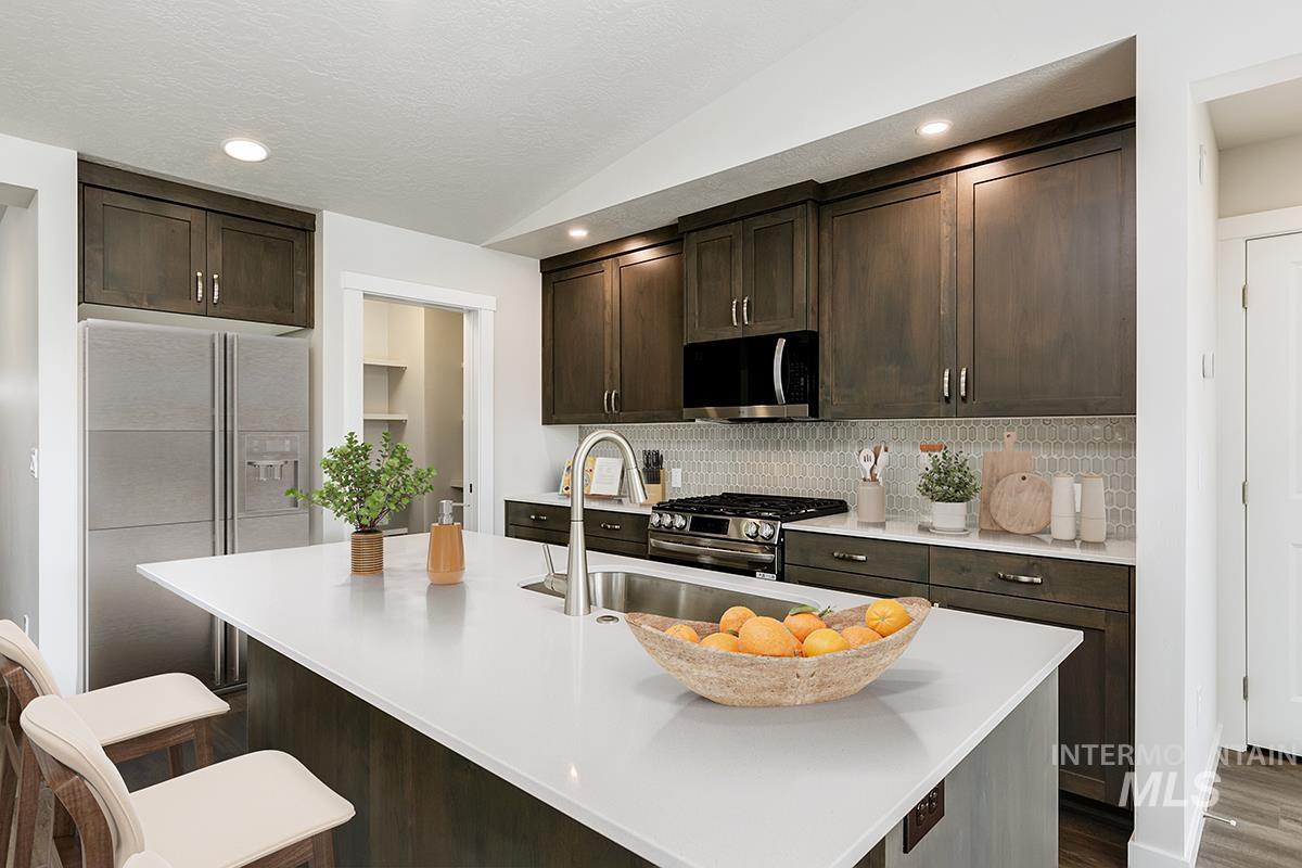 7080 South Gamely Avenue Meridian, ID 83642 - Photo 6 of 30 Kitchen featuring dark wood finish cabinetry, stainless steel appliances, lofted ceiling, a kitchen bar, and an island with sink