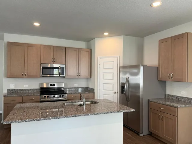 a kitchen with stainless steel appliances granite countertop a stove a sink a refrigerator white cabinets and wooden floor