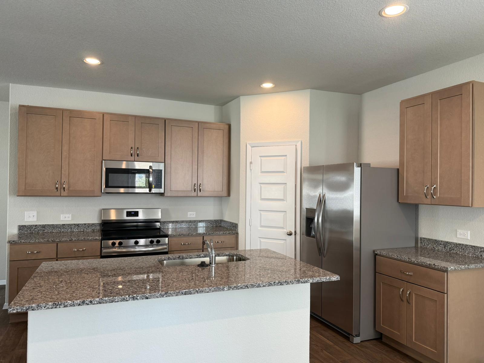 2601 Totley Road Pflugerville, TX 78660 - Photo 12 of 40 Kitchen with appliances with stainless steel finishes, dark wood finished floors, dark stone countertops, an island with sink, and recessed lighting