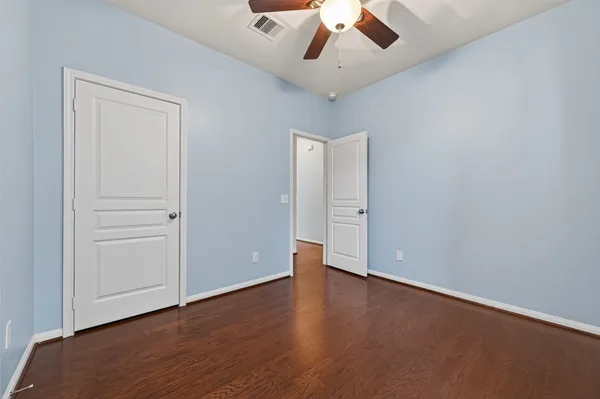 an empty room with wooden floor chandelier fan and windows