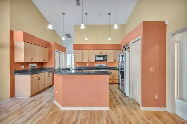 a kitchen with stainless steel appliances granite countertop a refrigerator a sink dishwasher a stove and a dining table with wooden floor