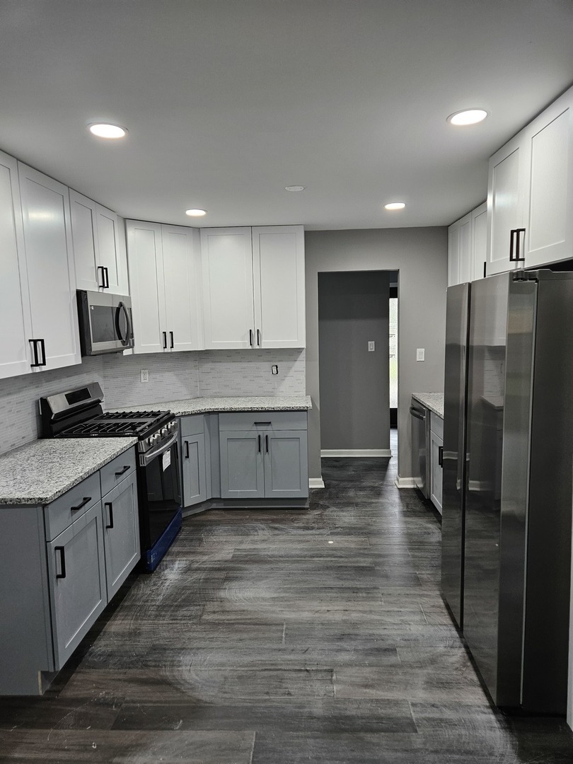 17612 Wright Street Lansing, IL 60438 - Photo 11 of 40 a large kitchen with stainless steel appliances granite countertop a stove a sink a refrigerator and white cabinets with wooden floor