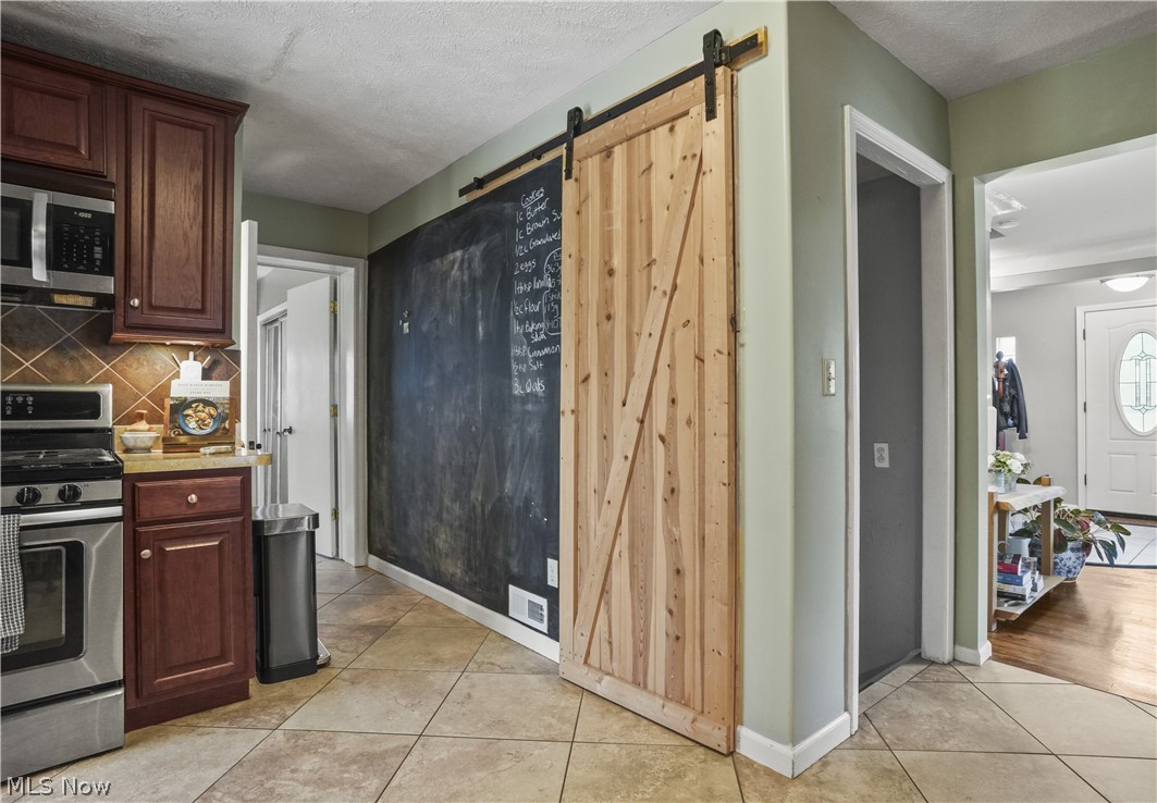 2122 Campus Road Cleveland, OH 44121 - Photo 12 of 39 Kitchen featuring tasteful backsplash, stainless steel appliances, a barn door, a textured ceiling, and light tile floors