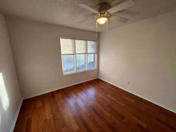 an empty room with wooden floor fan and windows