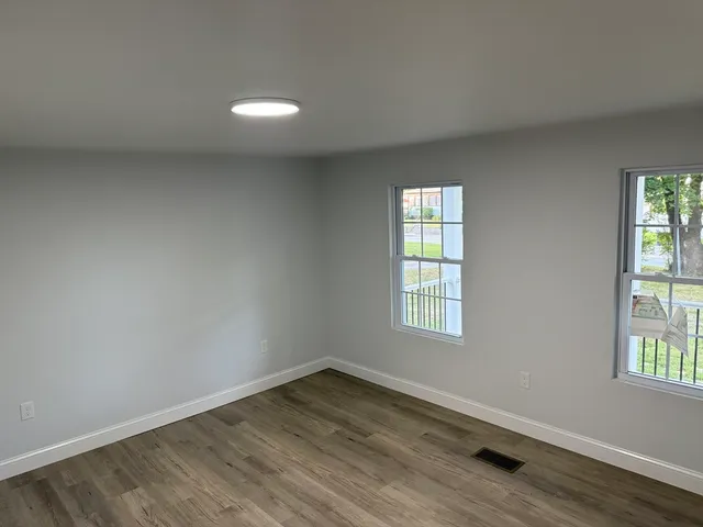 an empty room with wooden floor closet and windows