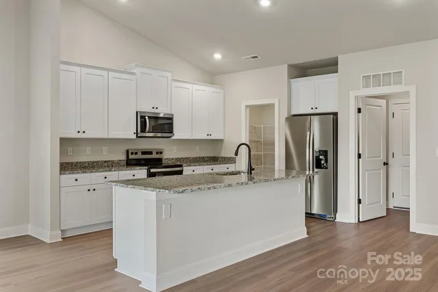 a kitchen with stainless steel appliances granite countertop a refrigerator a stove top oven a sink and dishwasher with wooden floor