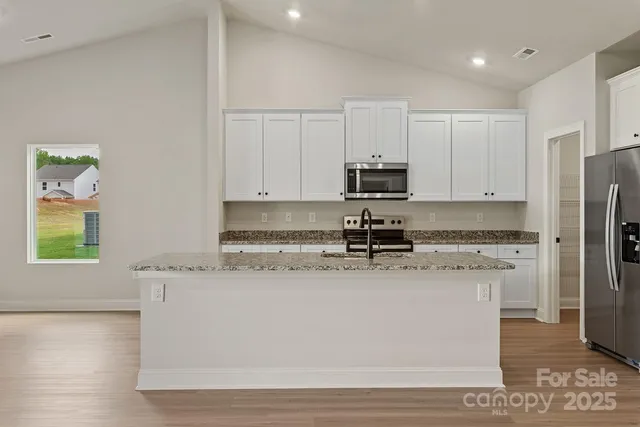 a kitchen with stainless steel appliances granite countertop a stove a sink a refrigerator a microwave and white cabinets