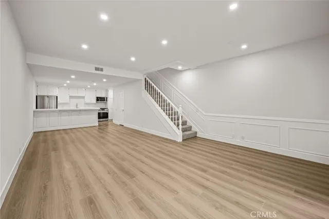 a view of an empty room with wooden floor kitchen view and a window